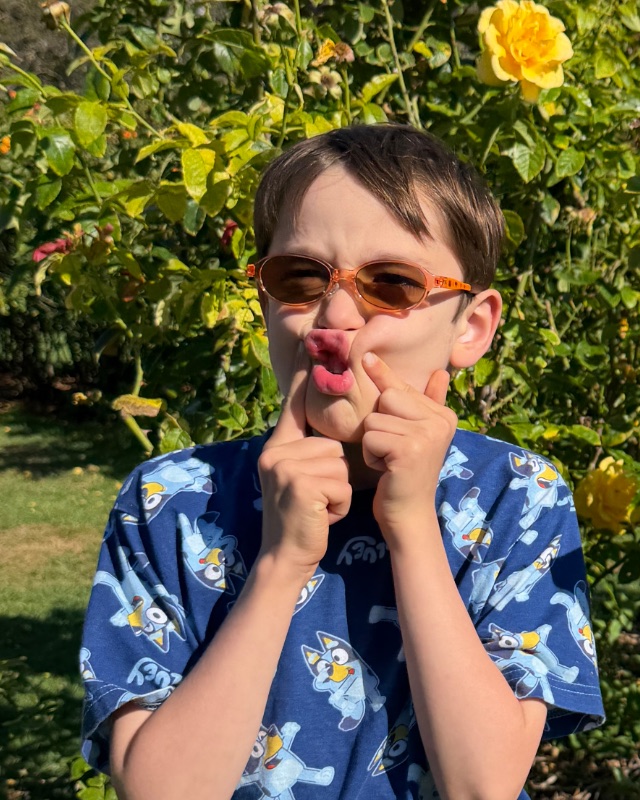 Alex in orange sunglasses in a rose garden, puckering his lips and pressing his cheeks.